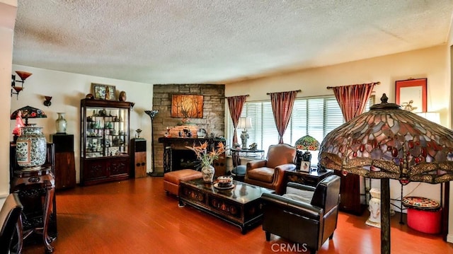 living area featuring a textured ceiling, wood finished floors, and a stone fireplace