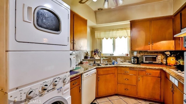 kitchen with brown cabinets, a sink, white dishwasher, and stacked washing maching and dryer