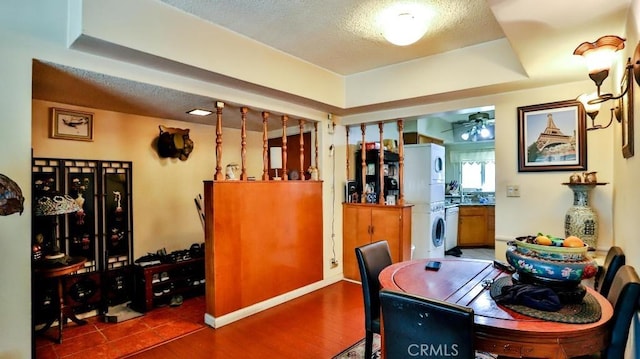 dining area with ceiling fan, a textured ceiling, a raised ceiling, and stacked washer / drying machine