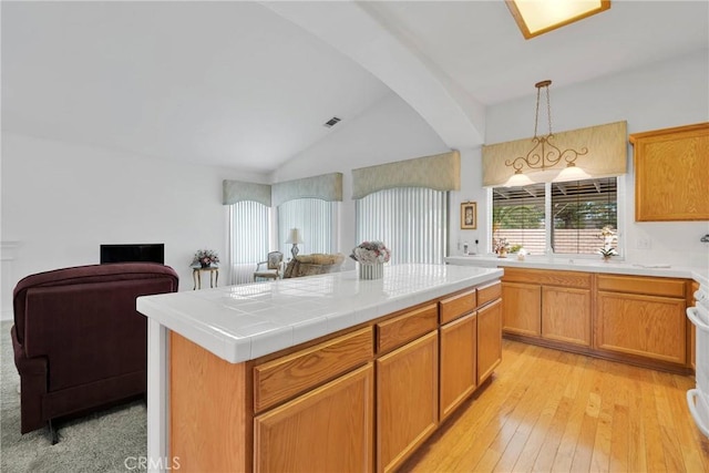 kitchen featuring tile countertops, lofted ceiling, pendant lighting, a center island, and light wood-type flooring