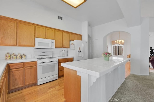 kitchen with hanging light fixtures, white appliances, light hardwood / wood-style floors, a center island, and an inviting chandelier