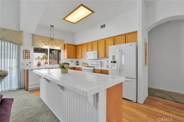 kitchen featuring tile countertops, a center island, light hardwood / wood-style flooring, decorative light fixtures, and white appliances