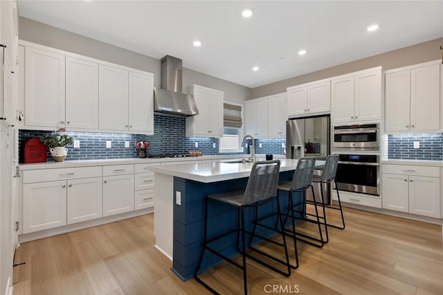 27717 Knoll View Pl, Valencia, CA 91381 - kitchen featuring wall chimney range hood, a sink, light wood-style floors, white cabinetry, and decorative backsplash