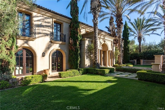 view of front of home featuring a balcony, stucco siding, a front yard, and french doors