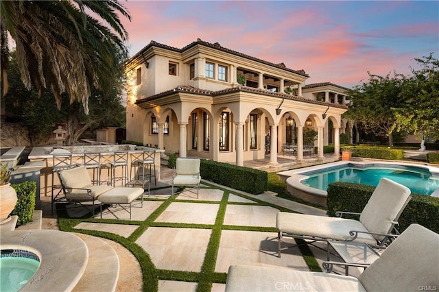 back of property at dusk featuring an in ground hot tub, a tiled roof, stucco siding, an outdoor pool, and a patio area