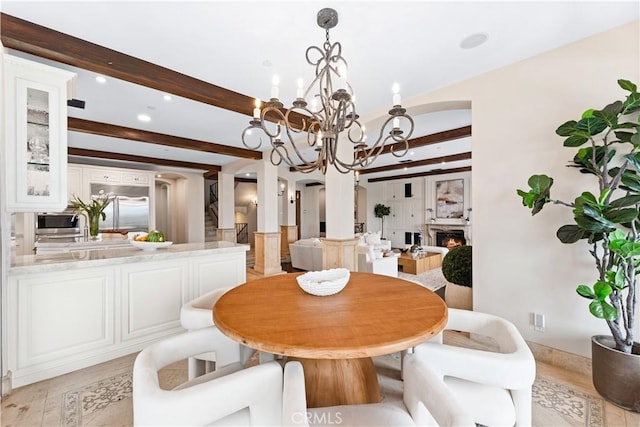 dining space with arched walkways, a notable chandelier, light wood-style floors, a lit fireplace, and beam ceiling