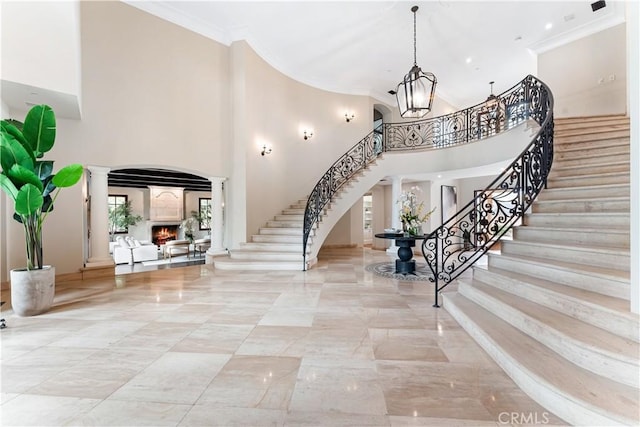 entryway featuring ornamental molding, a lit fireplace, ornate columns, and stairs