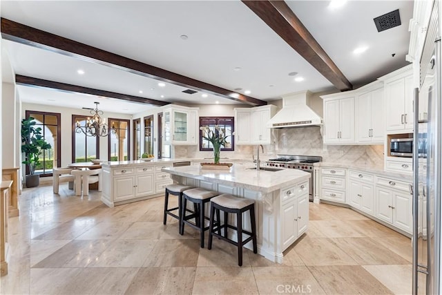 kitchen featuring tasteful backsplash, built in appliances, custom exhaust hood, a chandelier, and a sink