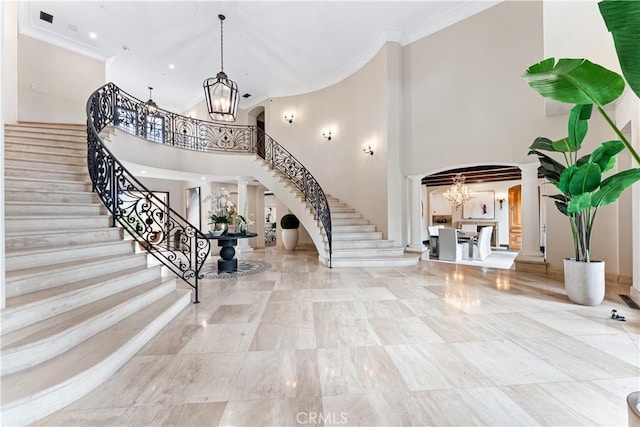 entrance foyer with decorative columns, arched walkways, ornamental molding, stairs, and a chandelier