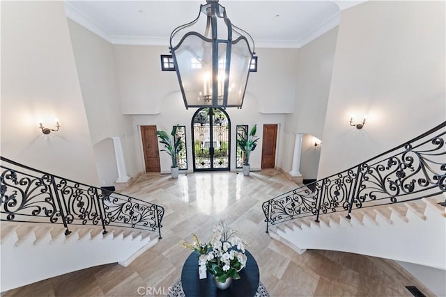 foyer entrance featuring a chandelier, ornamental molding, a towering ceiling, and decorative columns