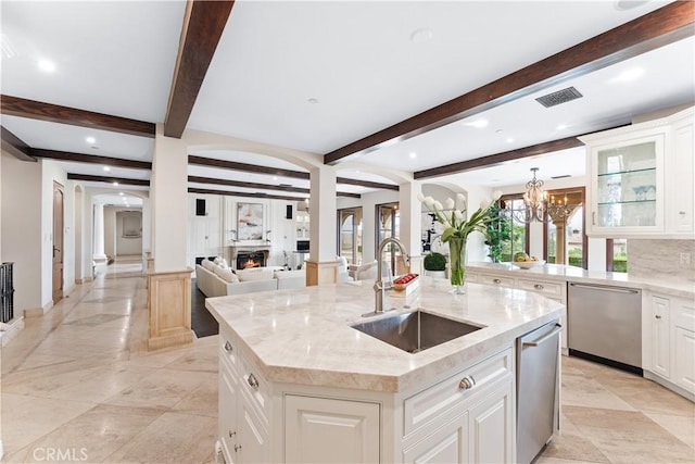 kitchen with a sink, a lit fireplace, light stone countertops, dishwasher, and a center island with sink