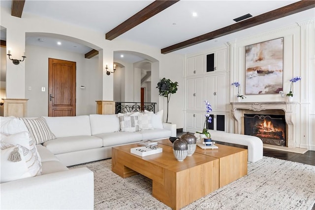 living area featuring visible vents, a fireplace, arched walkways, and beamed ceiling