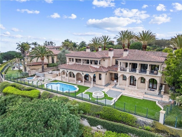 back of house with a fenced front yard, a yard, a balcony, and an in ground hot tub