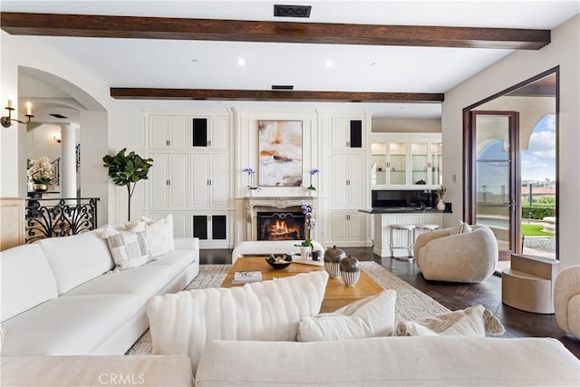 living room featuring arched walkways, wood finished floors, visible vents, beamed ceiling, and a glass covered fireplace