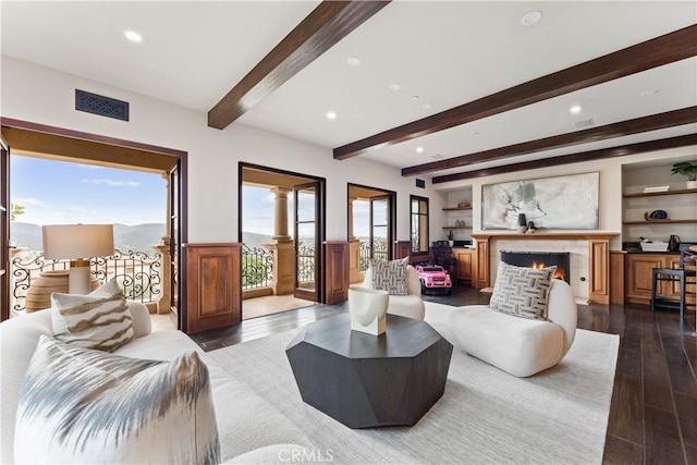 living area with beam ceiling, recessed lighting, visible vents, dark wood-type flooring, and a warm lit fireplace