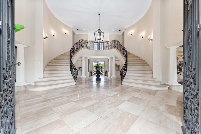 foyer entrance with a chandelier, a towering ceiling, stairs, decorative columns, and crown molding