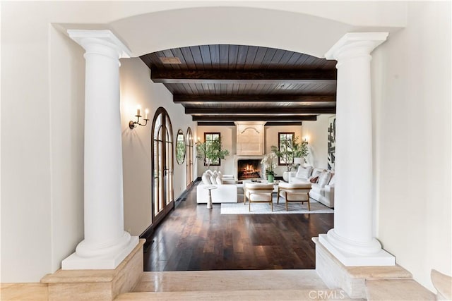 foyer entrance featuring wood ceiling, a warm lit fireplace, and decorative columns