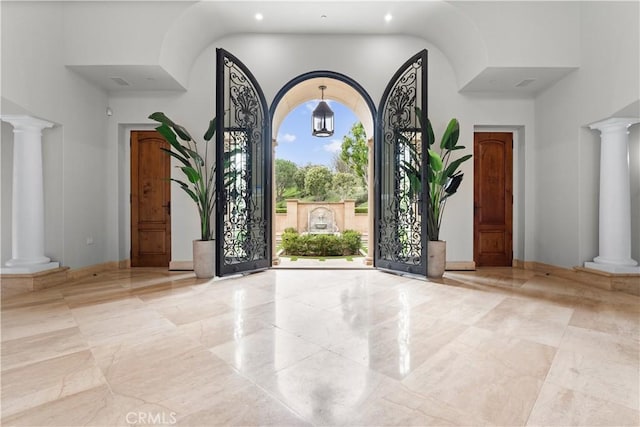 foyer entrance featuring marble finish floor, a towering ceiling, and ornate columns