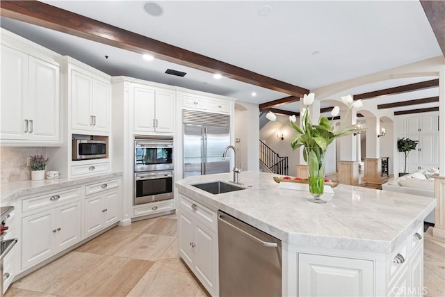 kitchen with arched walkways, a kitchen island with sink, stainless steel appliances, a sink, and white cabinets