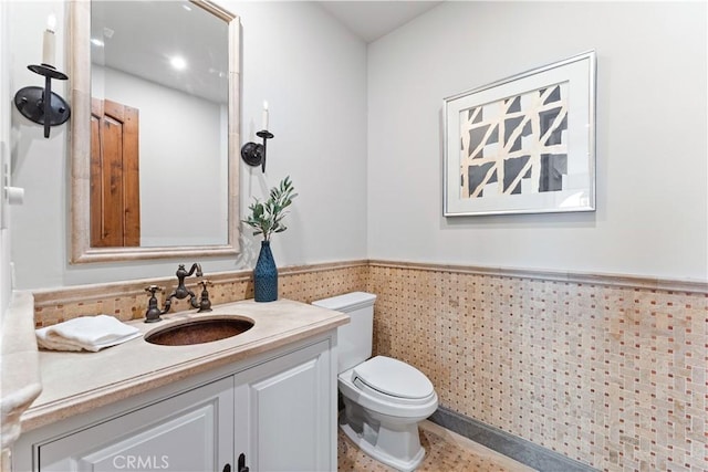 bathroom featuring toilet, vanity, tile walls, and wainscoting