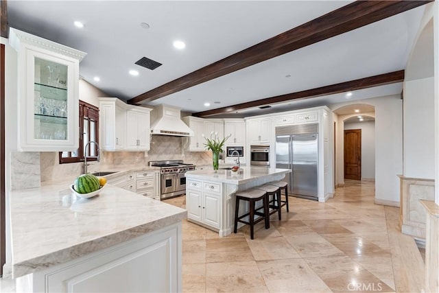 kitchen with arched walkways, high quality appliances, a kitchen breakfast bar, custom exhaust hood, and a sink