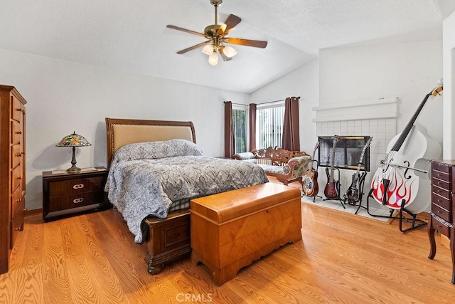 bedroom with ceiling fan, light wood-style floors, a fireplace, a textured ceiling, and lofted ceiling