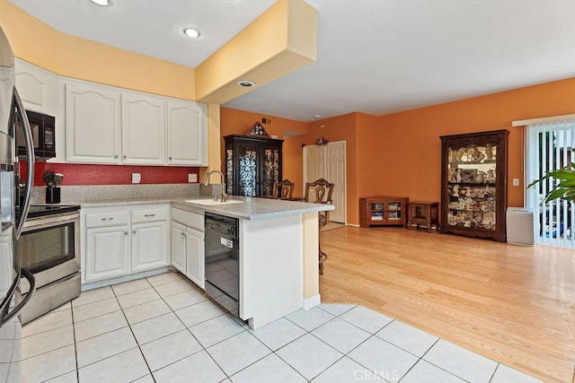 kitchen featuring a peninsula, light countertops, white cabinetry, black appliances, and a sink
