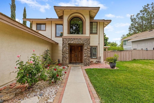 doorway to property featuring a yard, stone siding, and fence