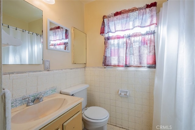 bathroom featuring toilet, a wainscoted wall, vanity, and tile walls