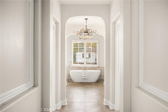 hall with light tile patterned floors, arched walkways, and an inviting chandelier