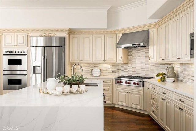 kitchen with wall chimney range hood, cream cabinets, stainless steel appliances, and crown molding