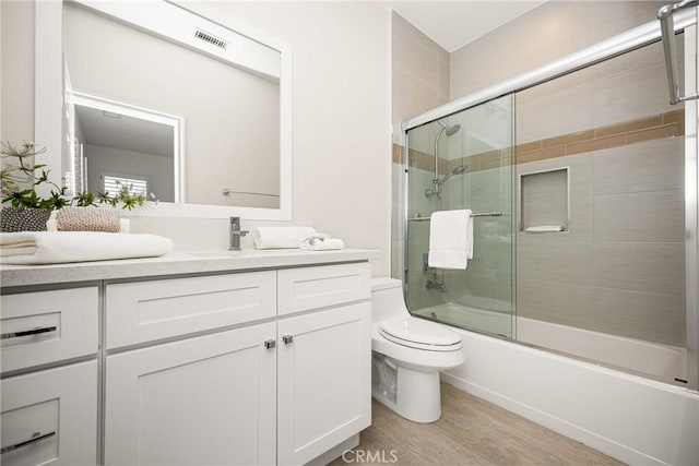 bathroom featuring toilet, shower / bath combination with glass door, wood finished floors, vanity, and visible vents