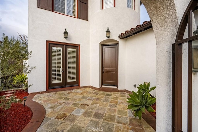 entrance to property with french doors, a patio area, a tiled roof, and stucco siding