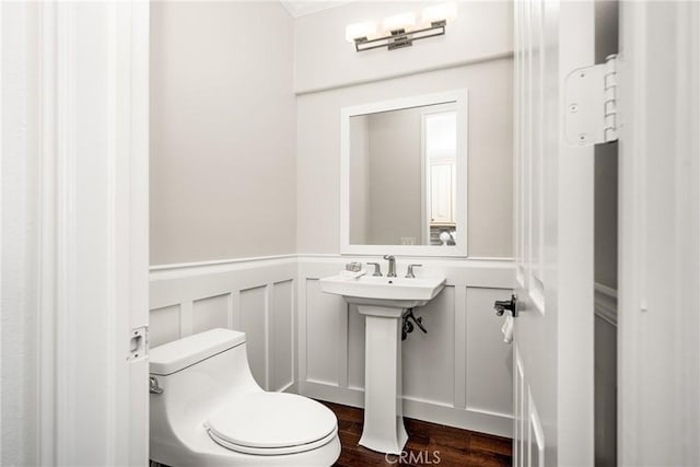 half bath with toilet, a wainscoted wall, a decorative wall, and wood finished floors