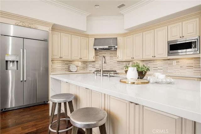 kitchen with cream cabinetry, wall chimney exhaust hood, and built in appliances