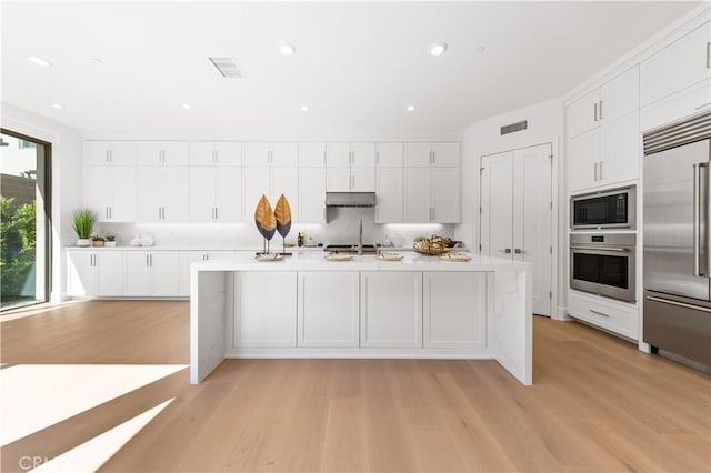 122 Appian Blvd, Irvine, CA 92602 - kitchen with light wood finished floors, light countertops, visible vents, built in appliances, and white cabinetry