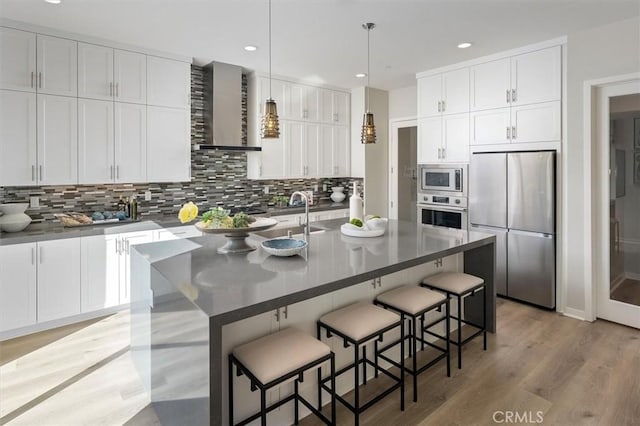 kitchen featuring a center island with sink, appliances with stainless steel finishes, white cabinetry, and wall chimney exhaust hood