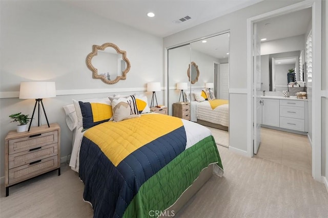 bedroom with connected bathroom, light carpet, and a closet