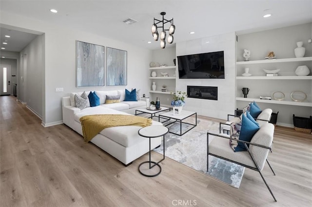 living room with a fireplace, a chandelier, light hardwood / wood-style floors, and built in features
