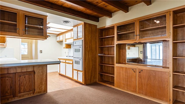 kitchen with light carpet, beamed ceiling, double oven, and wood ceiling