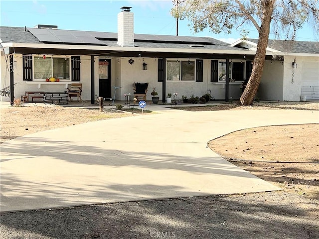 back of house with roof mounted solar panels, a chimney, driveway, and stucco siding