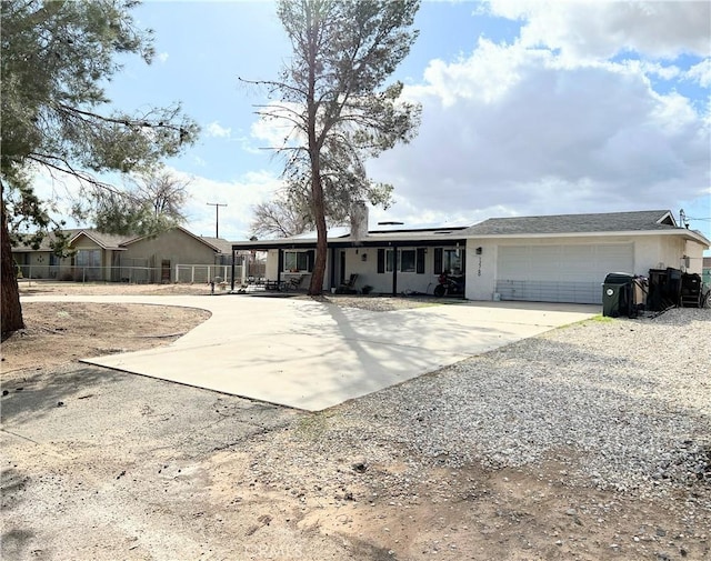 view of front of home with fence, concrete driveway, roof mounted solar panels, stucco siding, and a garage