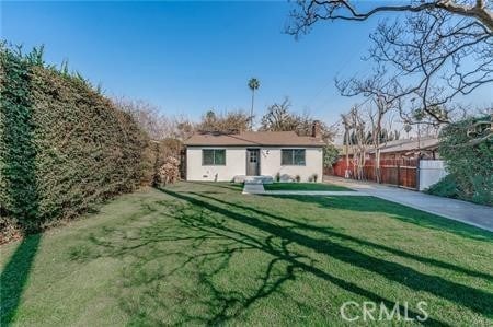 rear view of house with stucco siding, a yard, and fence