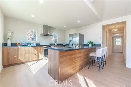 kitchen featuring an island with sink, light hardwood / wood-style floors, sink, a kitchen breakfast bar, and wall chimney exhaust hood