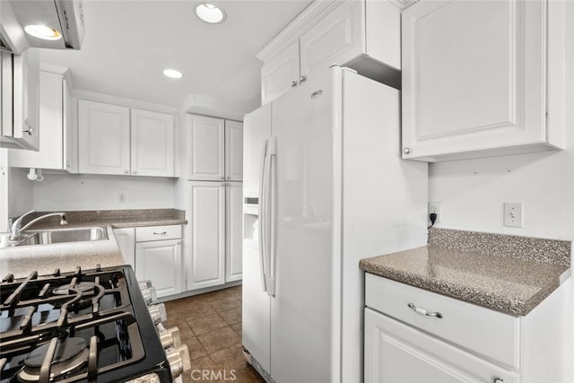 kitchen with white refrigerator with ice dispenser, sink, gas range oven, white cabinets, and dark tile patterned floors