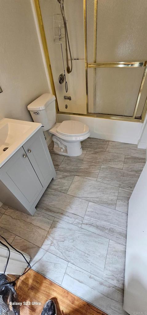 bathroom with enclosed tub / shower combo, toilet, and vanity