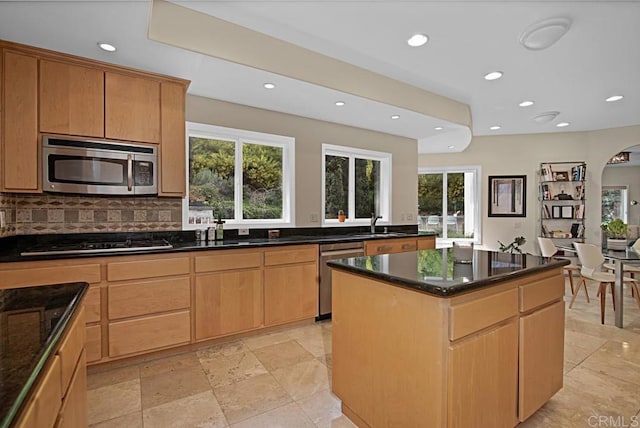 kitchen featuring stainless steel appliances, a kitchen island, sink, dark stone counters, and decorative backsplash