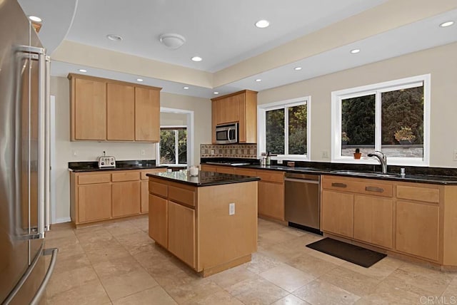 kitchen featuring stainless steel appliances, a kitchen island, sink, dark stone counters, and decorative backsplash