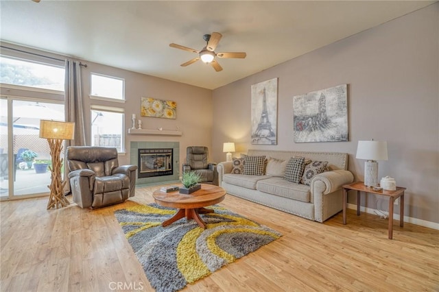 living room featuring baseboards, wood finished floors, a ceiling fan, and a tile fireplace