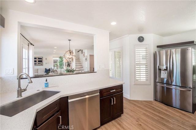 kitchen with appliances with stainless steel finishes, light hardwood / wood-style flooring, dark brown cabinets, pendant lighting, and sink